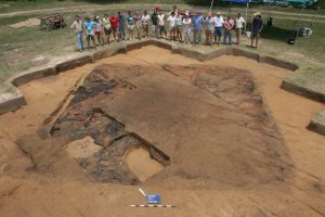 An archaeological digsite. People look on as an excavated building's foundation is displayed. 